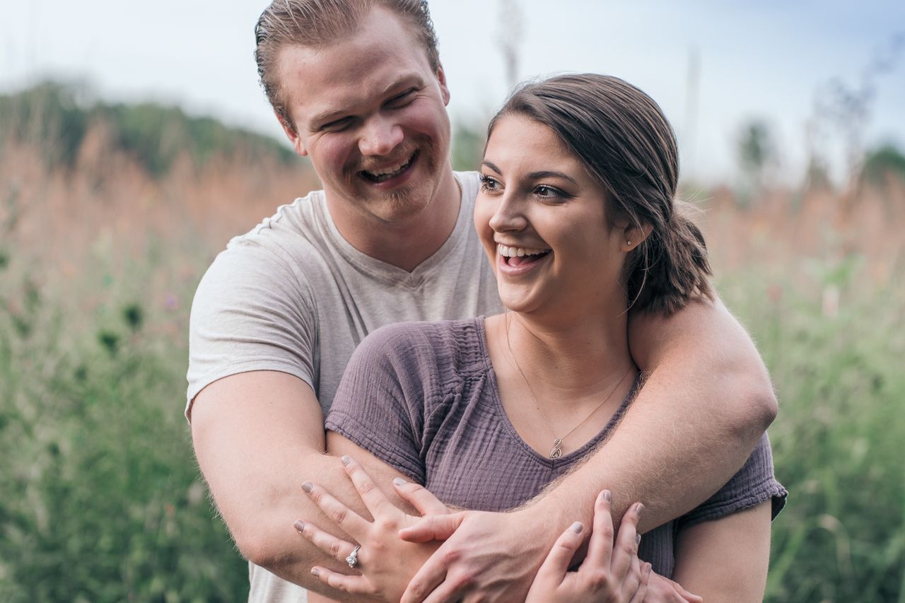 A joyful couple shares a candid laughing moment together in a field of tall grass. Marion, Ohio