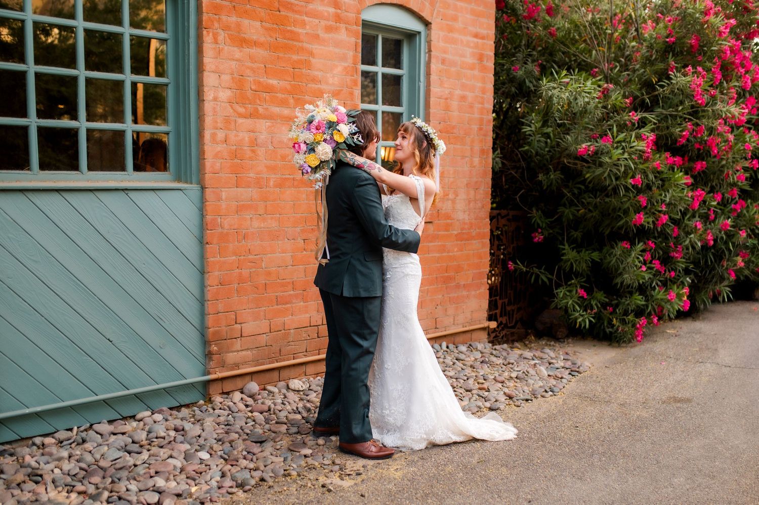 Bride and groom sharing romantic kiss under tall palm trees in sunlit outdoor wedding venue.