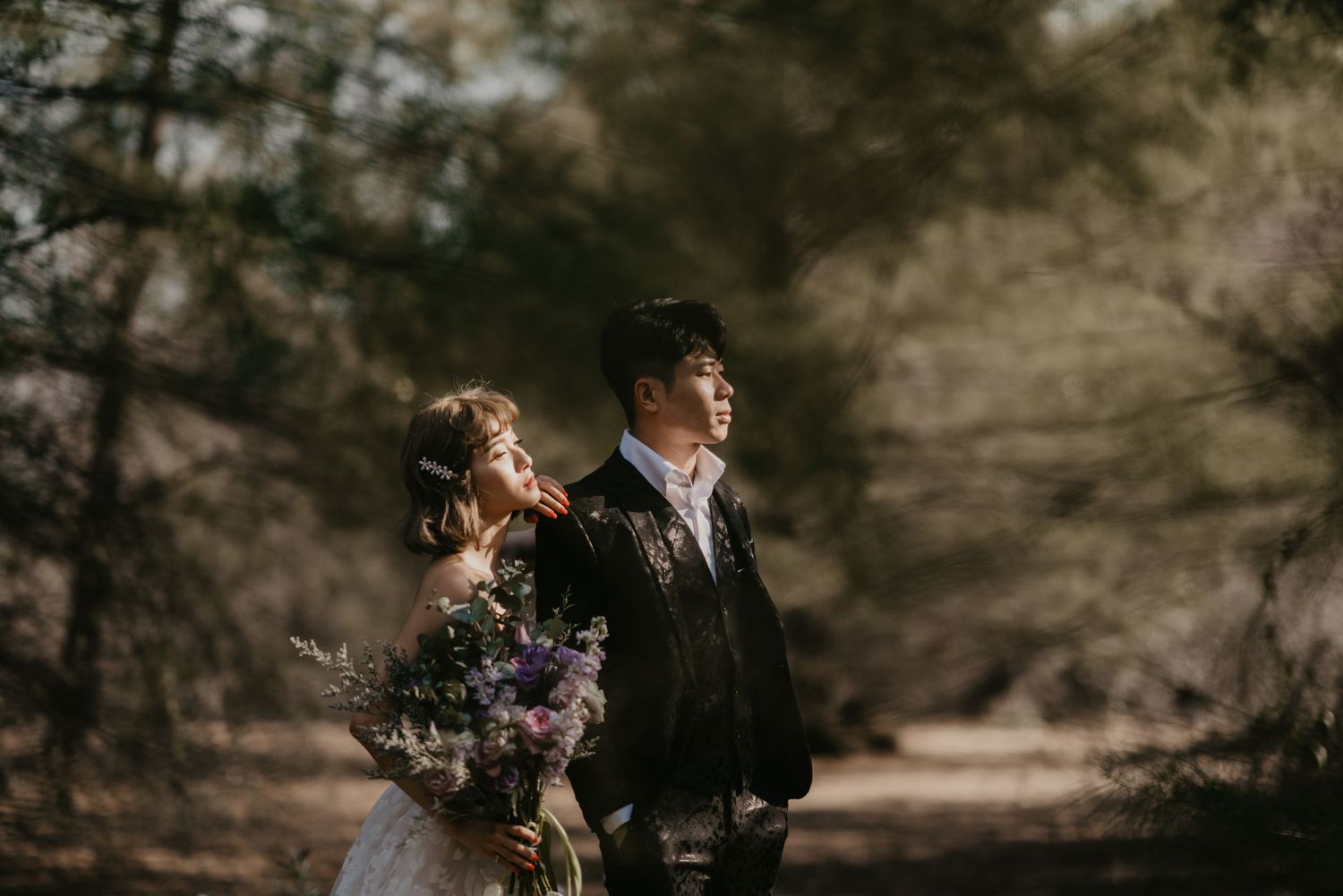 A couple embraces during their wedding photoshoot in a serene forest backdrop.