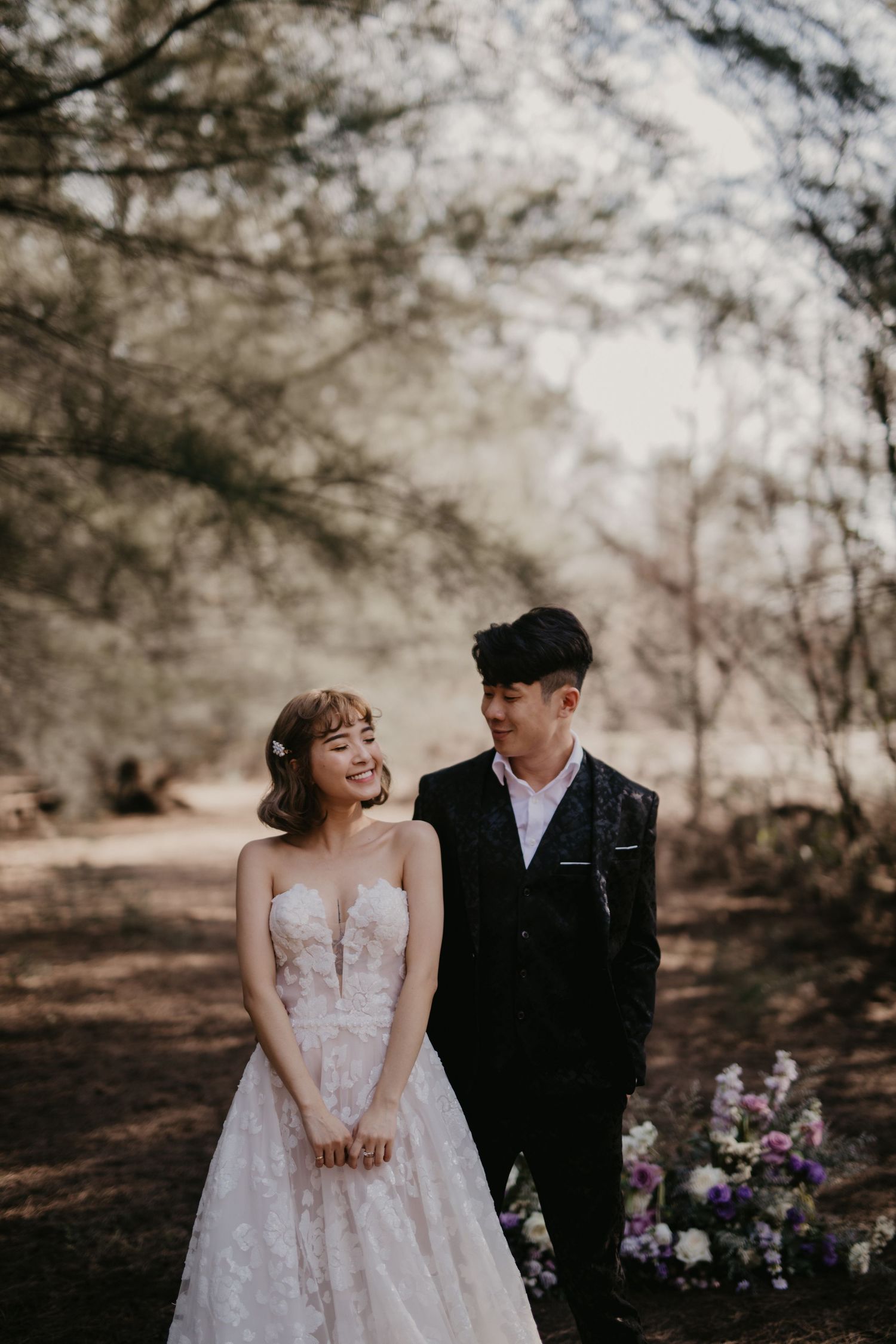Candid wedding moments captured in a forest with scattered purple floral arrangements.