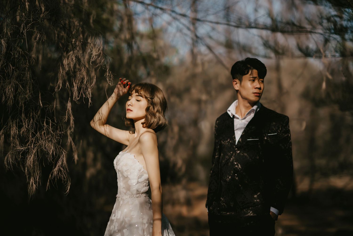 A romantic wedding photoshoot in a wooded area with a couple in formal attire.