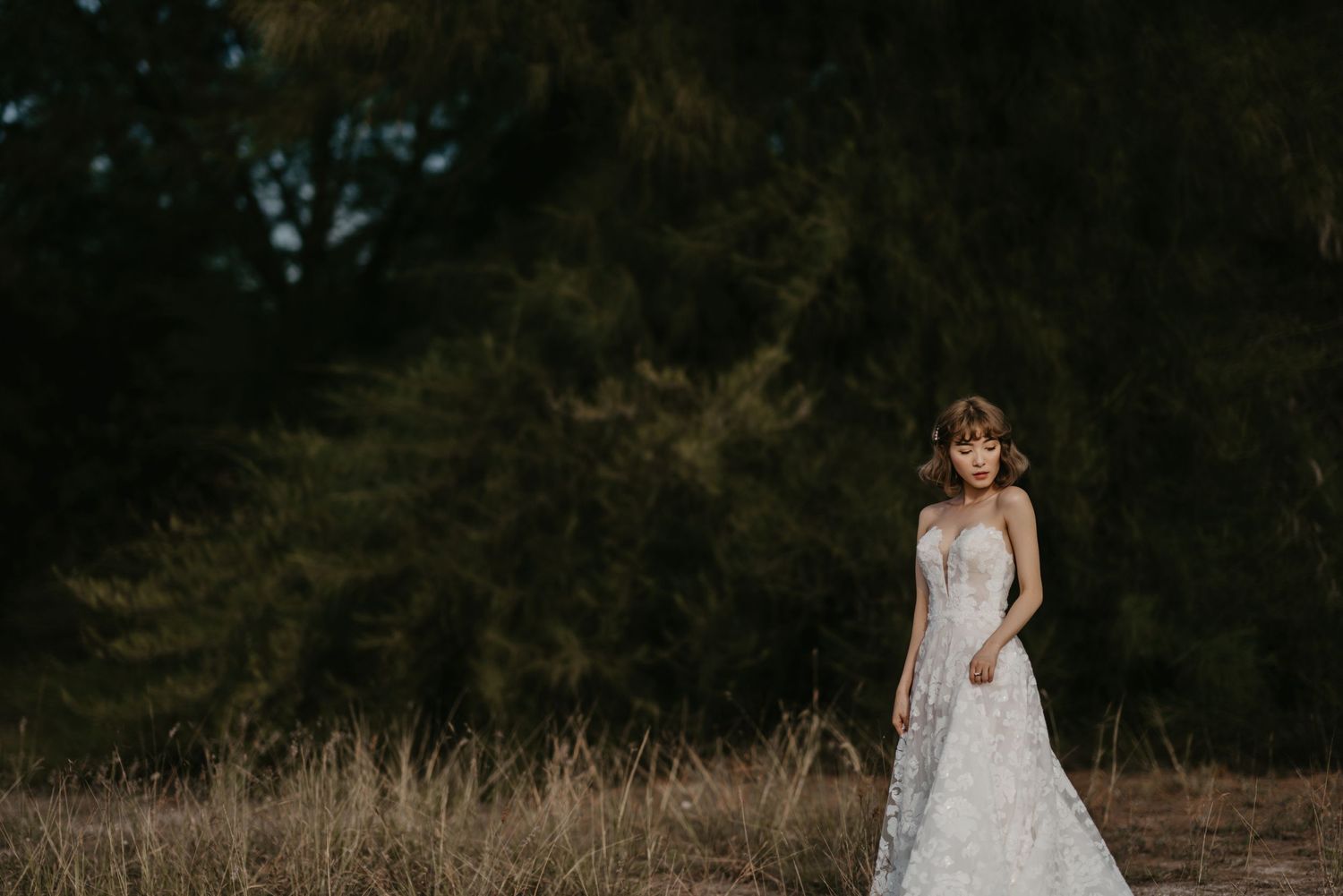 A bride in a lace wedding gown poses gracefully in a natural outdoor setting.
