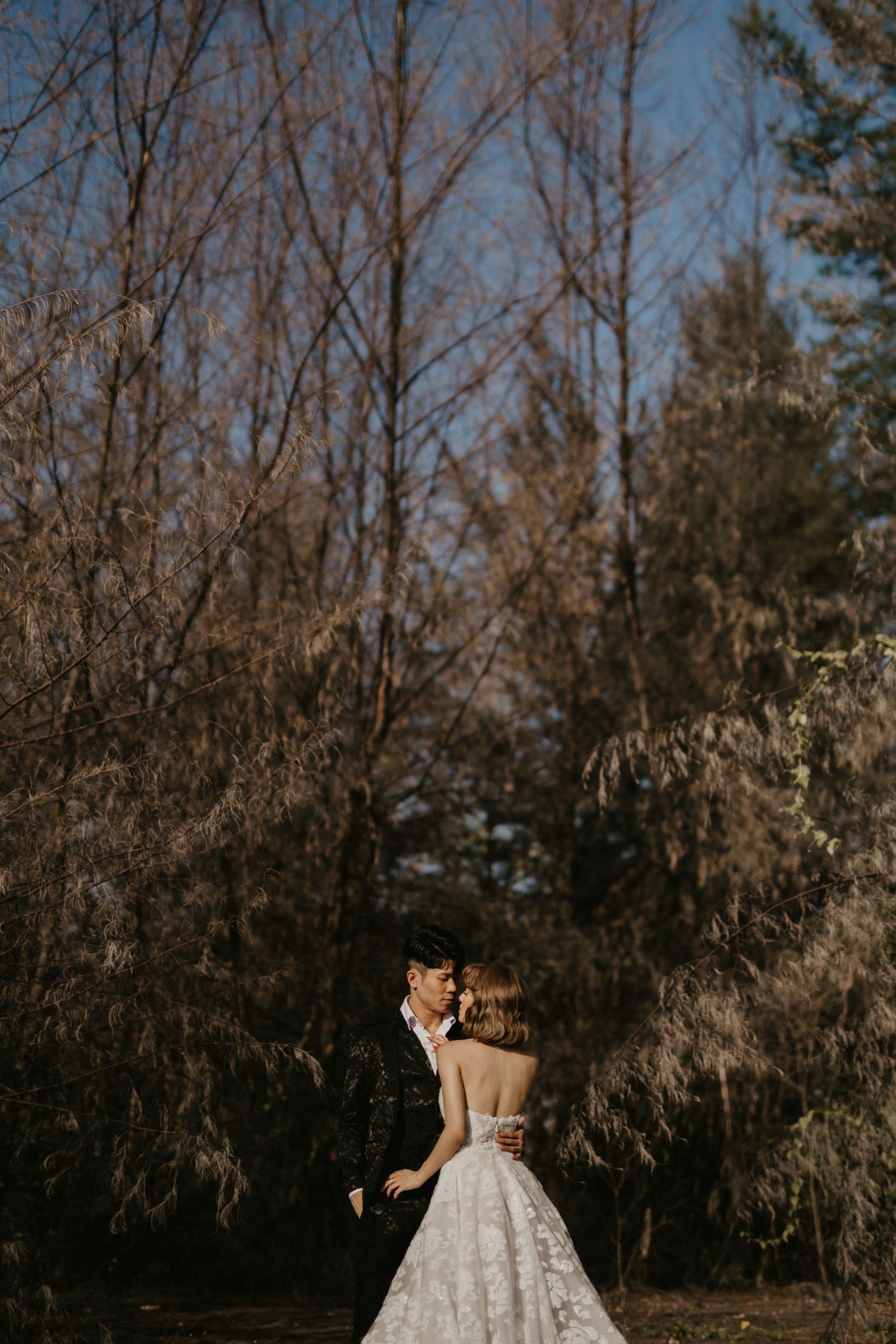 A romantic wedding couple embraces in a forest setting during golden hour.
