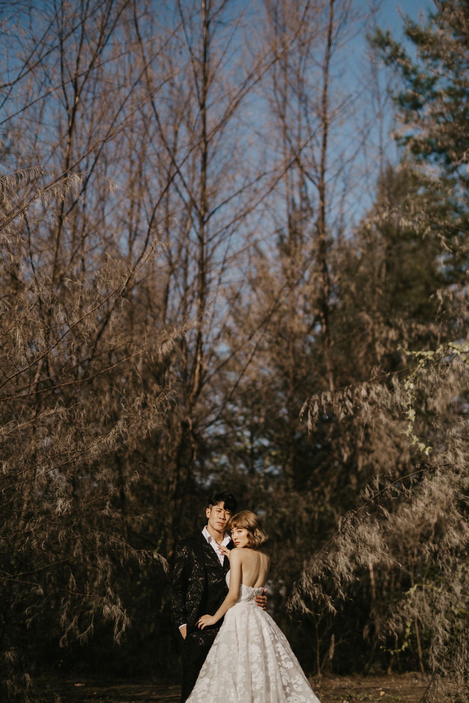 A couple shares an intimate moment surrounded by bare winter trees.