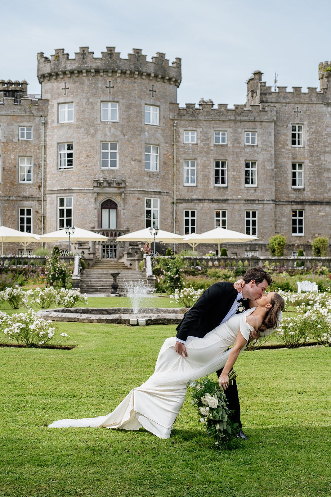 Romantic castle wedding photo with manicured gardens and stone architecture in the background, groom kissing bride in county Sligo, Ireland.