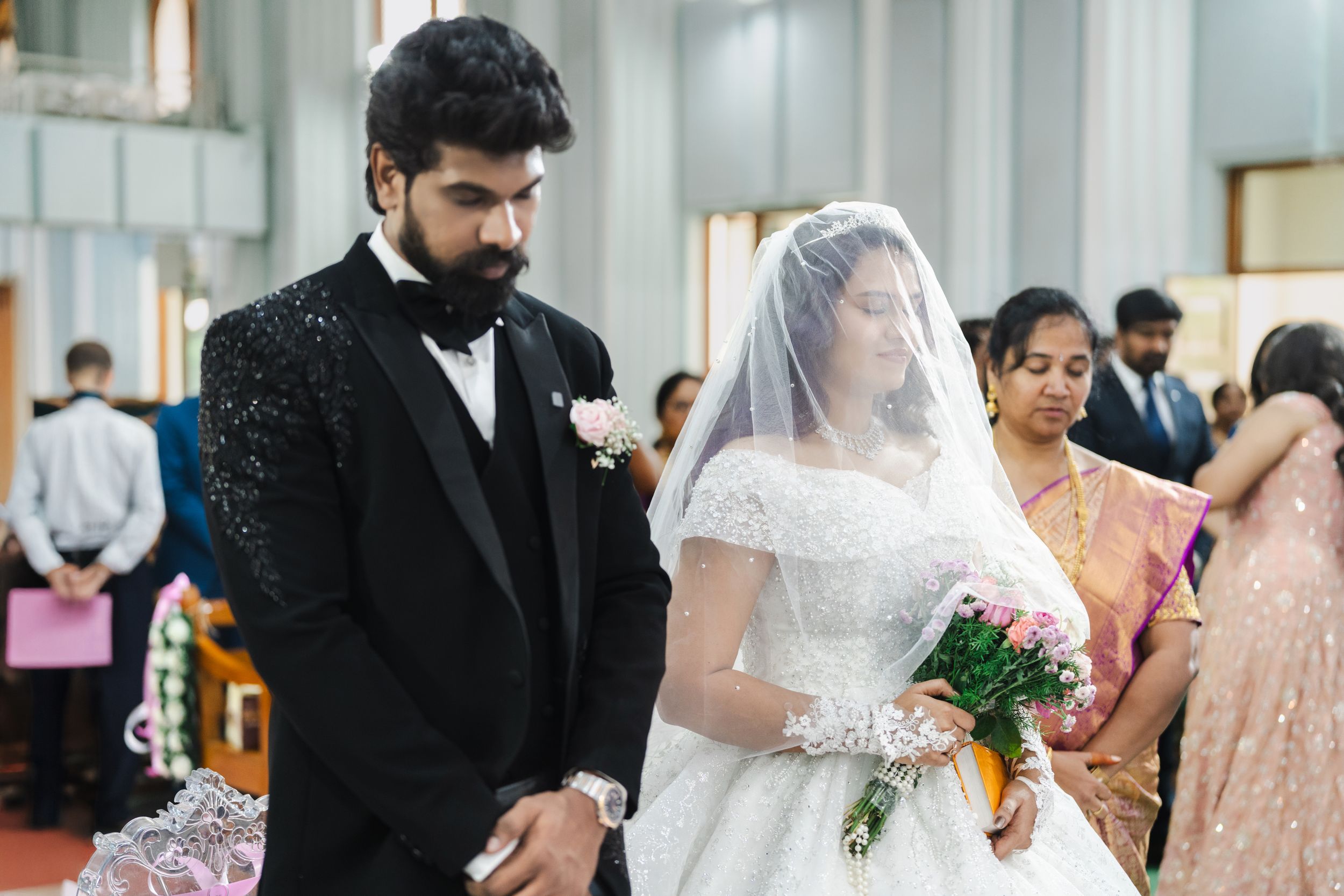 Bride in white gown and groom in black tuxedo stand at church altar during traditional Christian wedding ceremony.