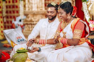Couple in traditional South Indian wedding attire performing ceremonial rituals with a coconut at their wedding.