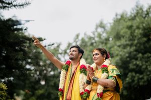 Two people in traditional Indian attire pointing and smiling outdoors during a celebration.