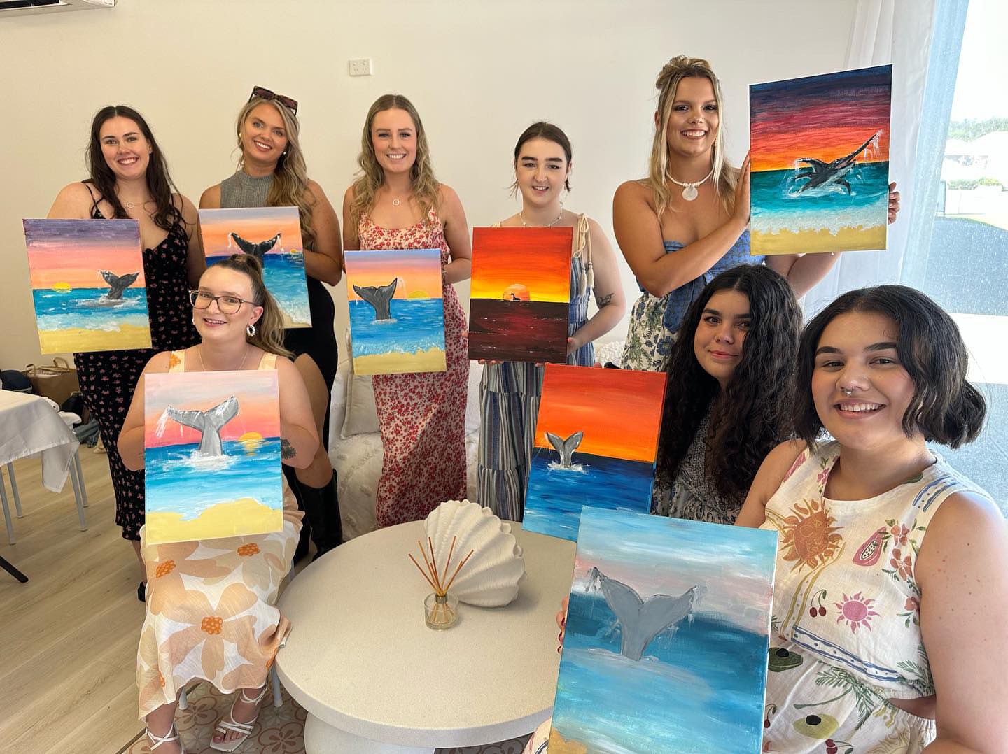 Group photo of art students displaying their completed beach sunset paintings.