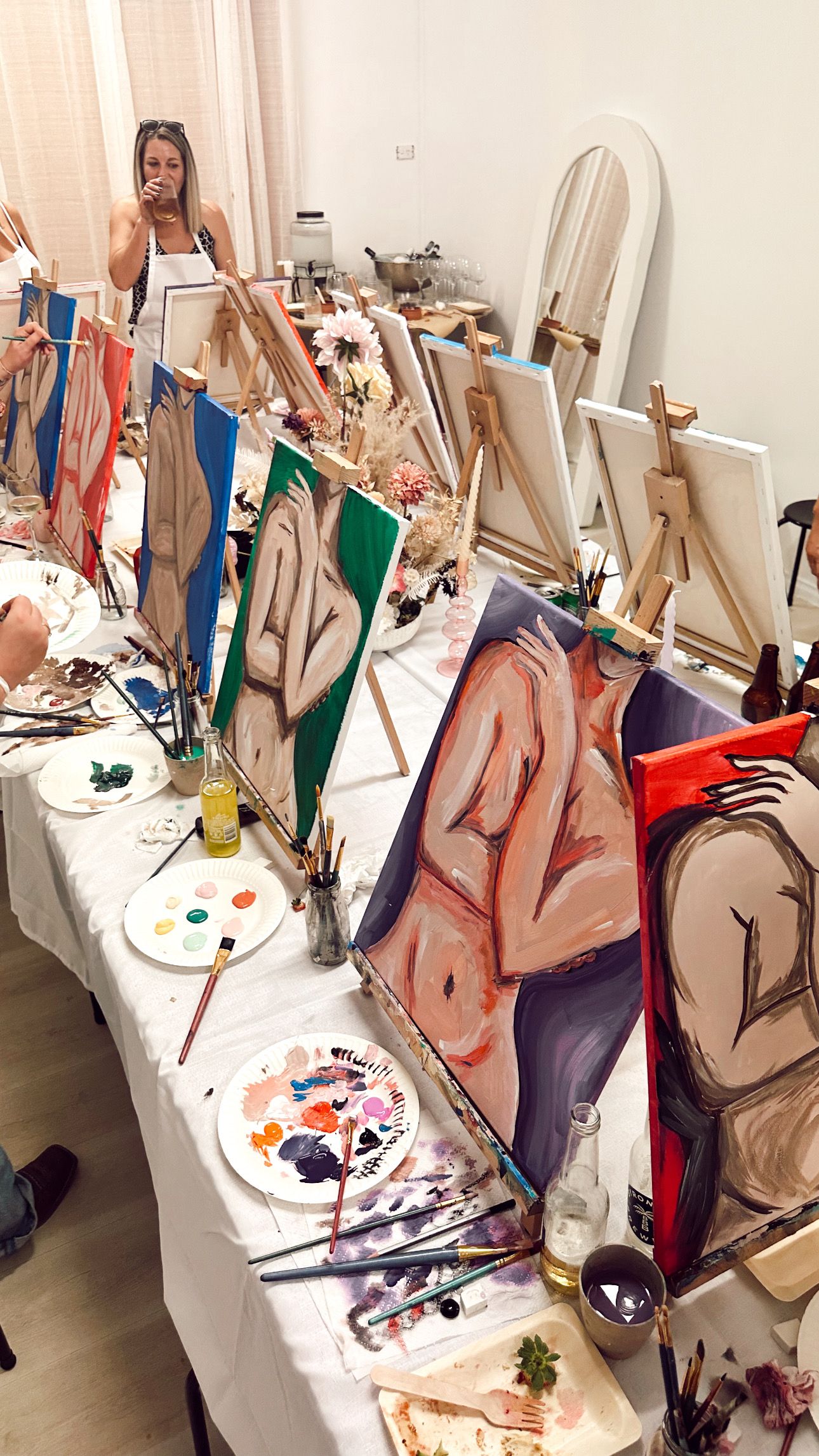 An art studio table covered with easels, paint palettes, and figure drawings in progress.