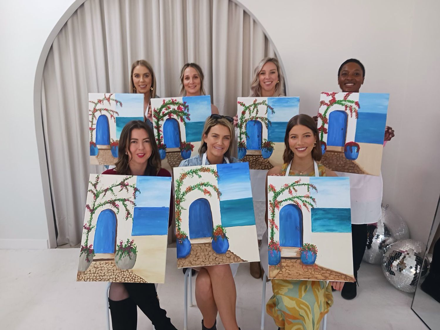 A group shows off their completed beach-themed paintings featuring bright blue archways during an art class.