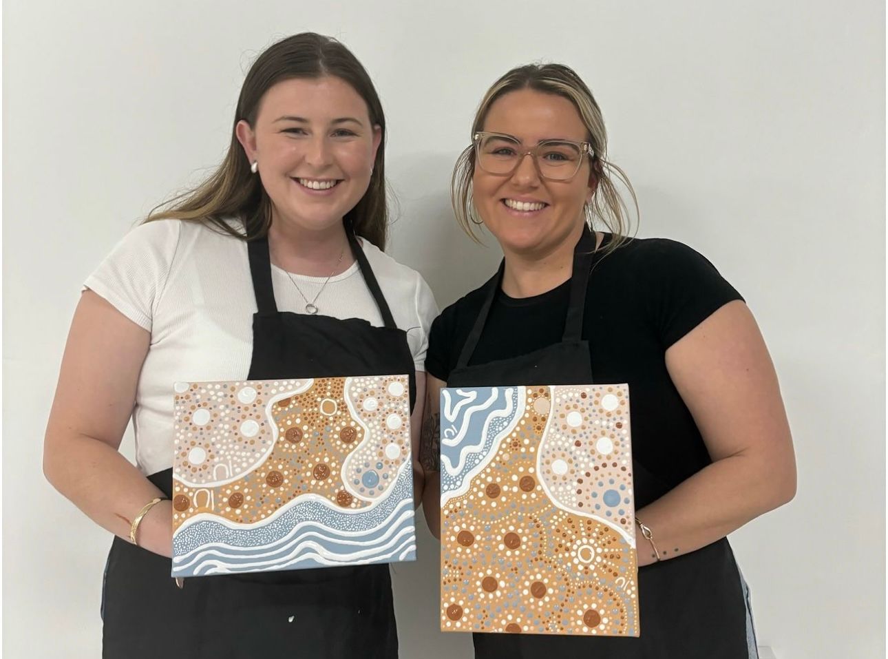 Two artists pose with their completed abstract coastal artwork featuring brown and blue patterns.