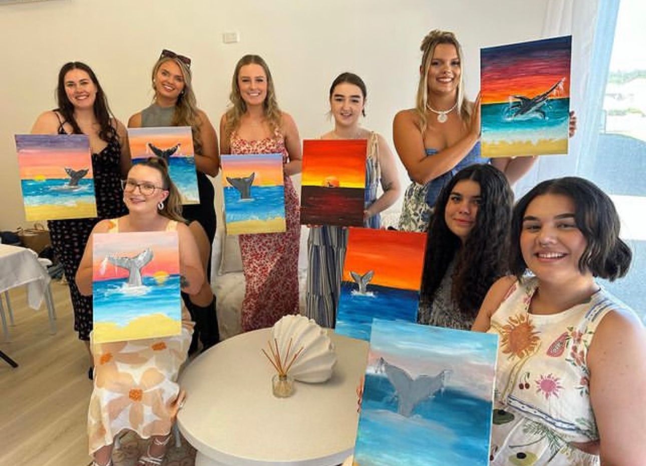 Students display their completed ocean sunset paintings during an art class.