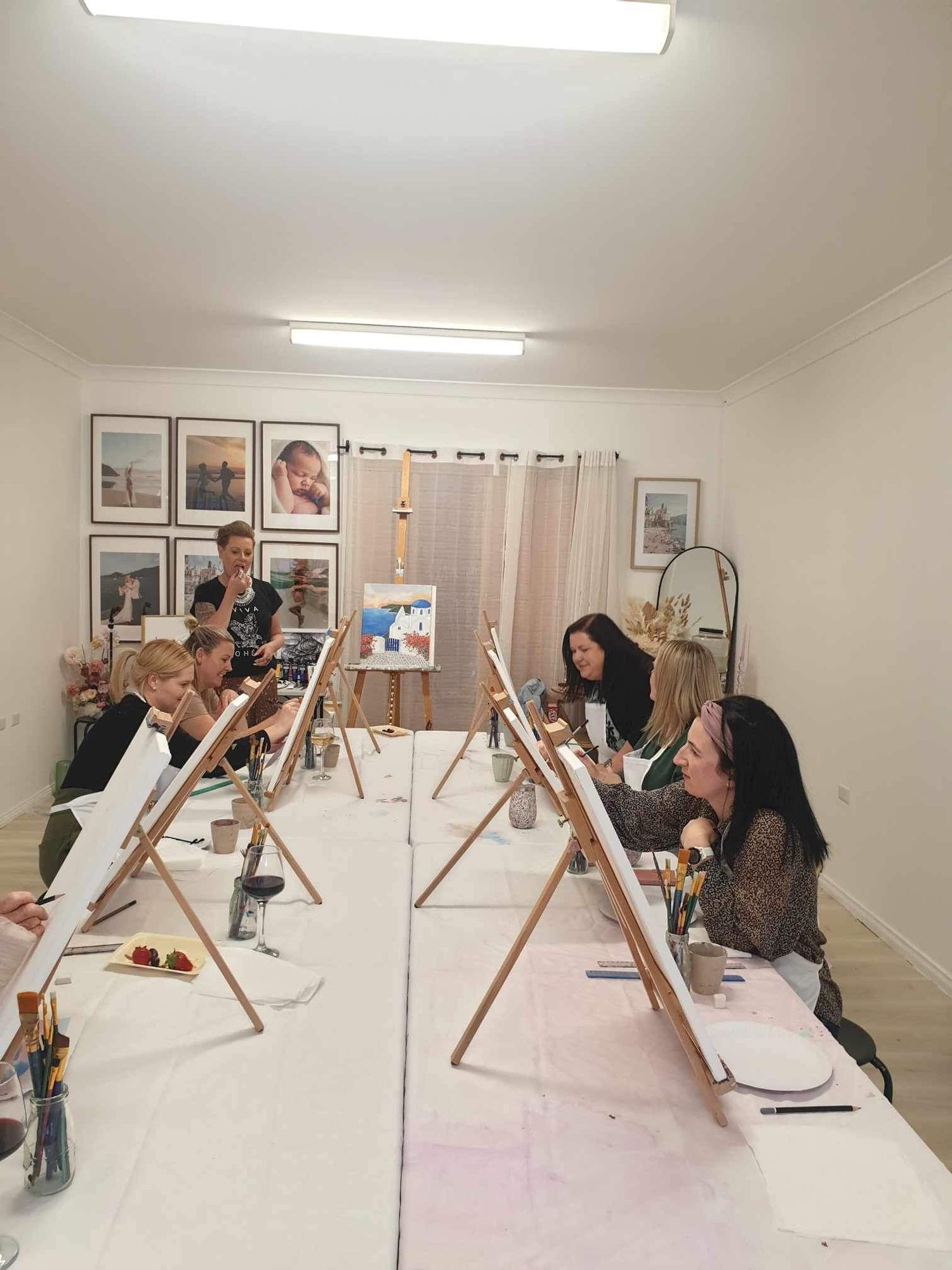 Art students working at wooden easels in a studio space with framed artwork on walls.