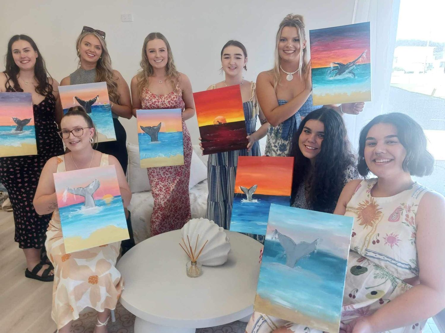 Students showing their completed beach sunset paintings during an art class.