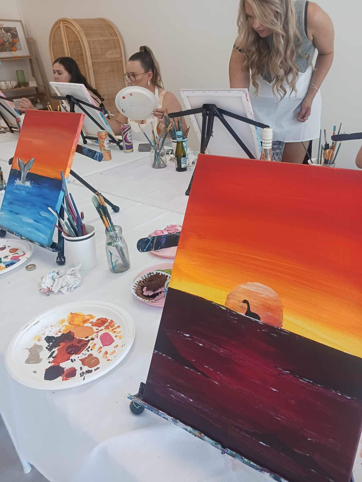Vibrant sunset painting in progress on easel with art supplies and palette in foreground.