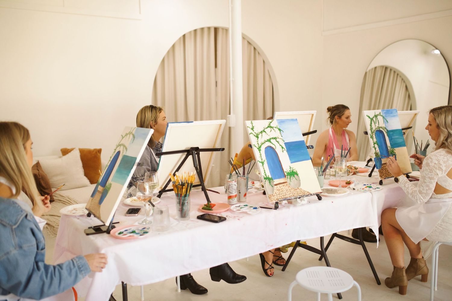 Group painting session with students at white tables in a bright studio space.