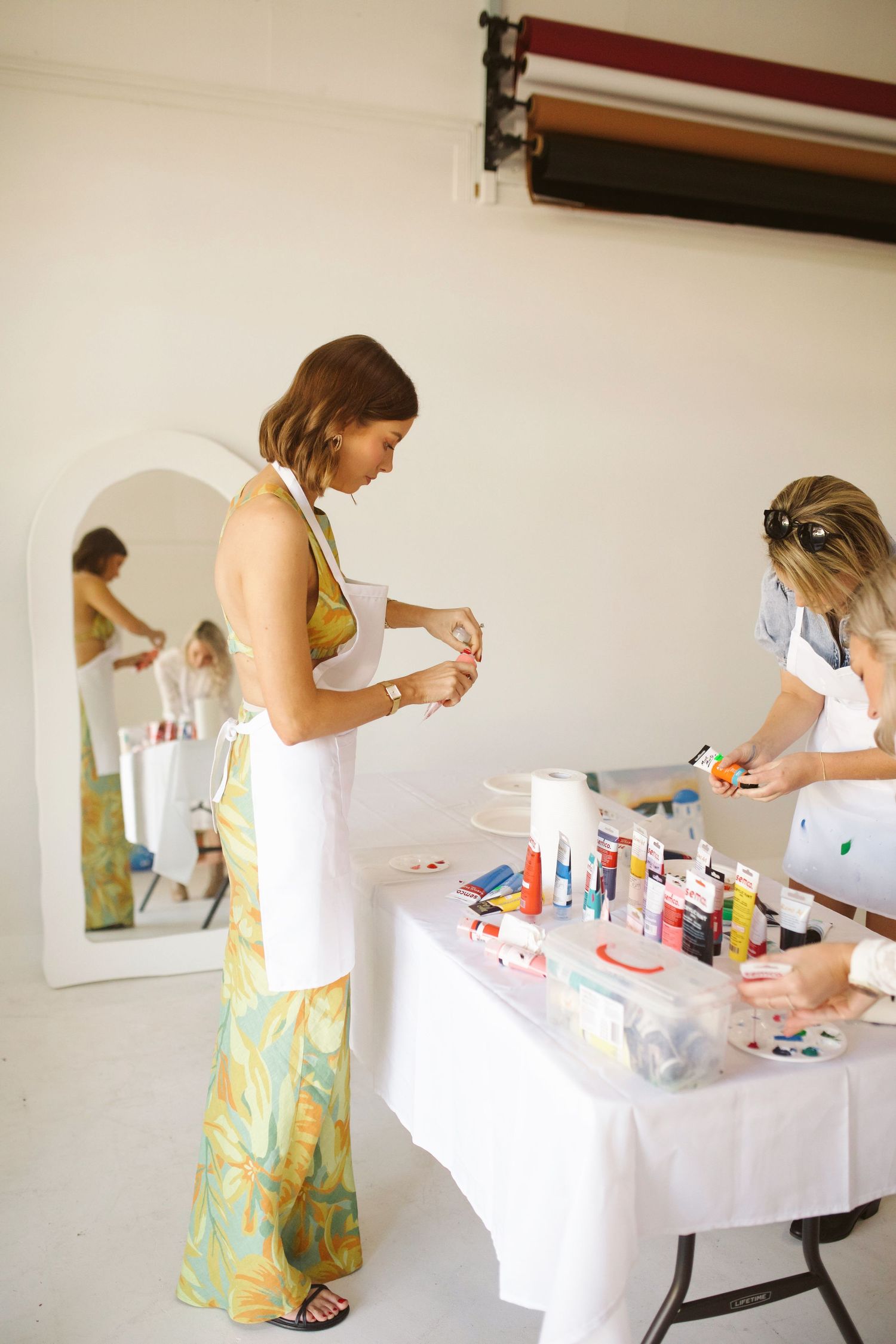 Women browsing art supplies at a creative workshop setup with white tables.