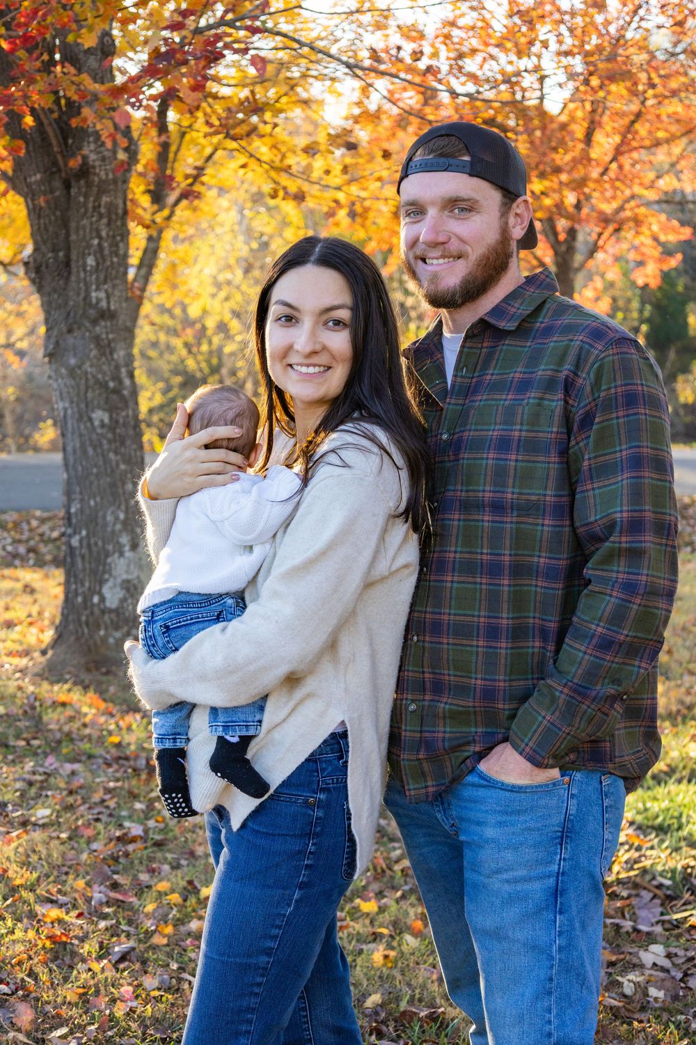 Happy young couple smiling outdoors in autumn park holding their newborn baby.