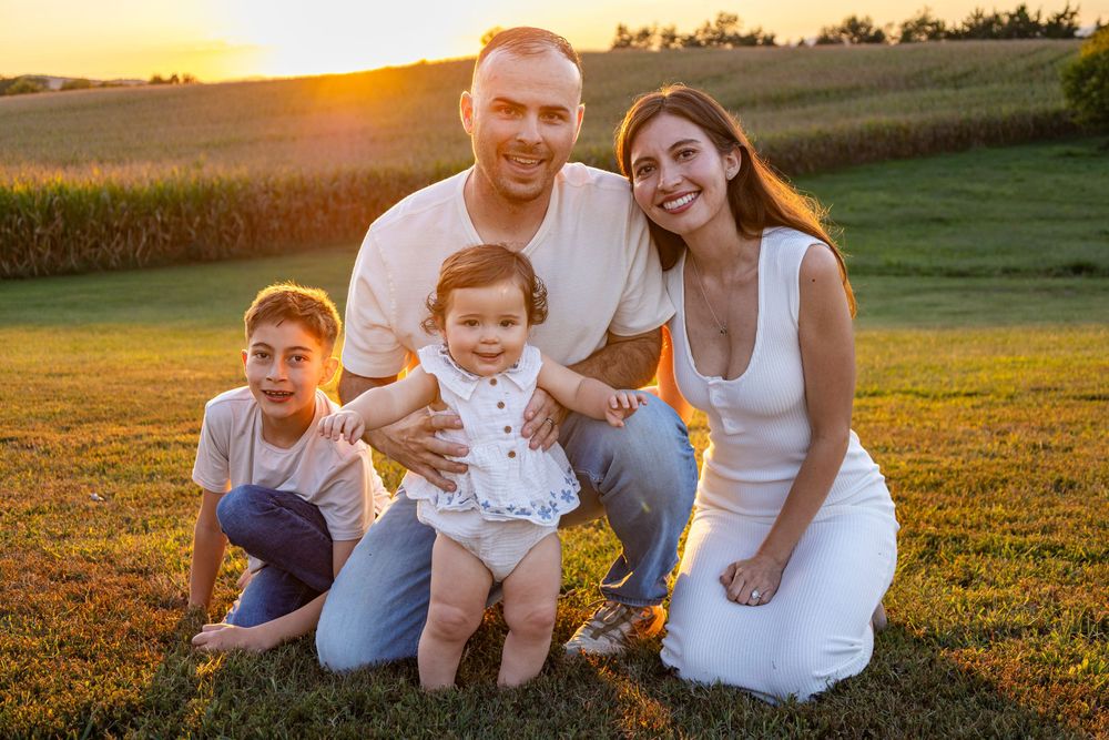 A family of four poses together smiling in a golden sunset field.