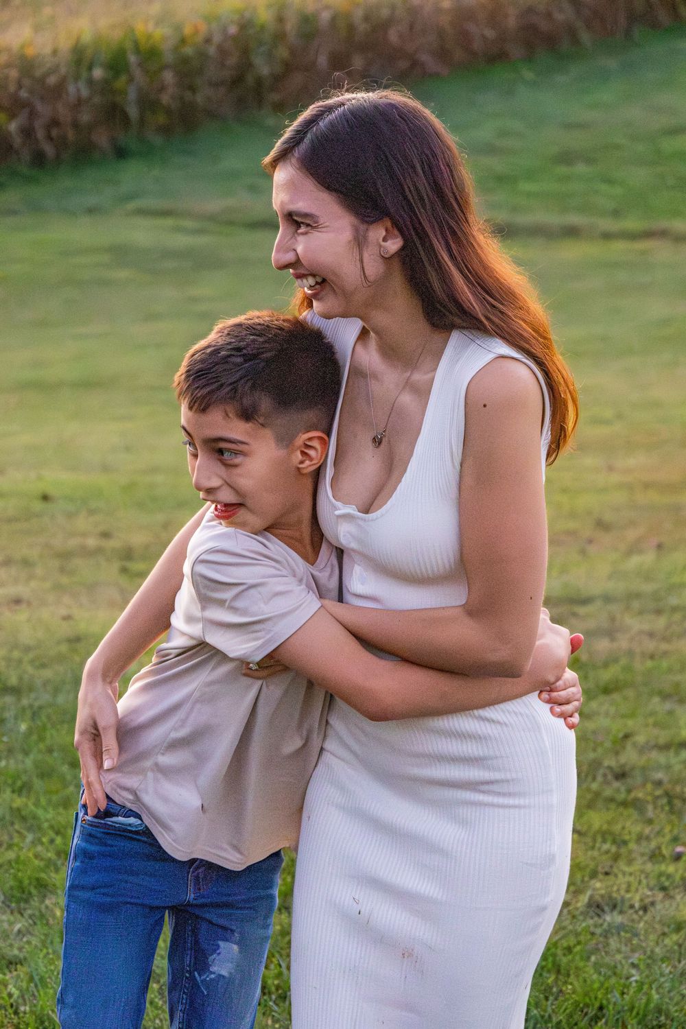 Happy mother and young son sharing a warm embrace while laughing outdoors on green grass.