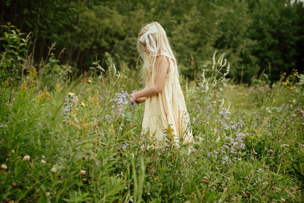 A figure in a white dress walks through a wildflower meadow on a sunny summer day.