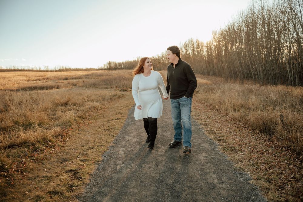 Two people walk hand in hand down a winding dirt path through golden autumn fields at sunset.