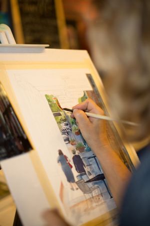Close-up of artist's hand painting a watercolor cityscape on canvas.