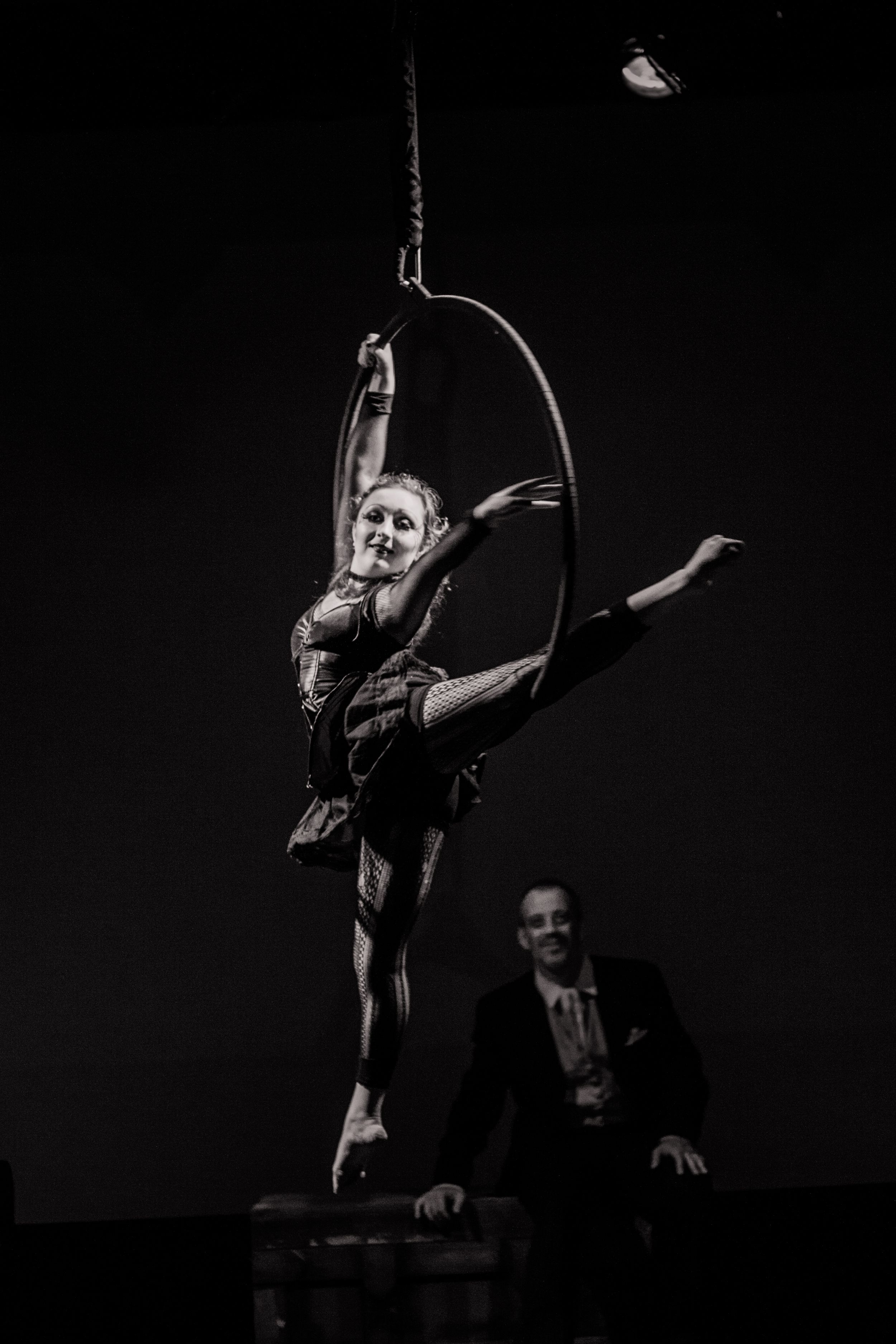 Aerial performer executes graceful pose on suspended equipment in dramatic black and white shot.