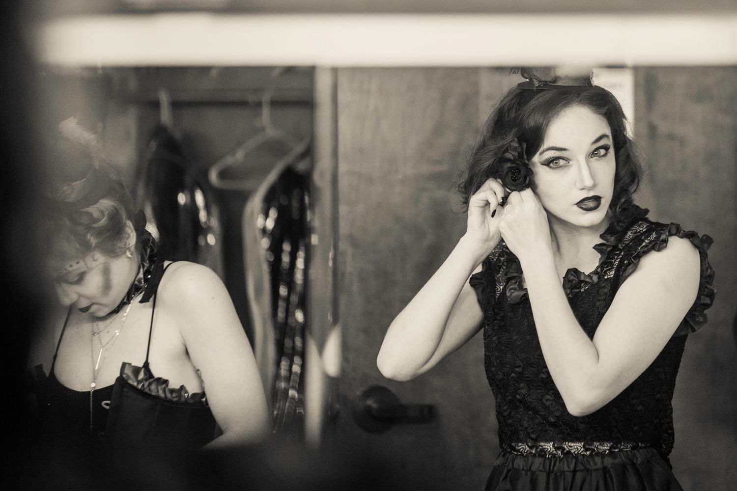 Vintage-style portrait of performer in black lace adjusting earrings backstage.