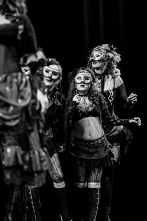 Gothic-styled performers in masks and vintage costumes pose dramatically in black and white.