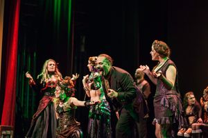 Performers in dark Victorian-style costumes dance together under theatrical lighting.