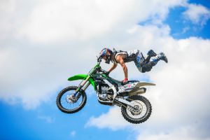 Motocross rider performs a daring freestyle jump against a blue sky with white clouds.