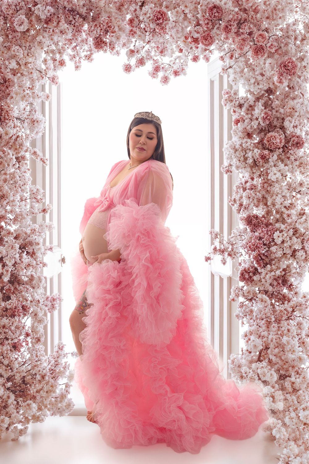 A dreamy maternity photoshoot with pink tulle dress against a backdrop of delicate cherry blossoms.