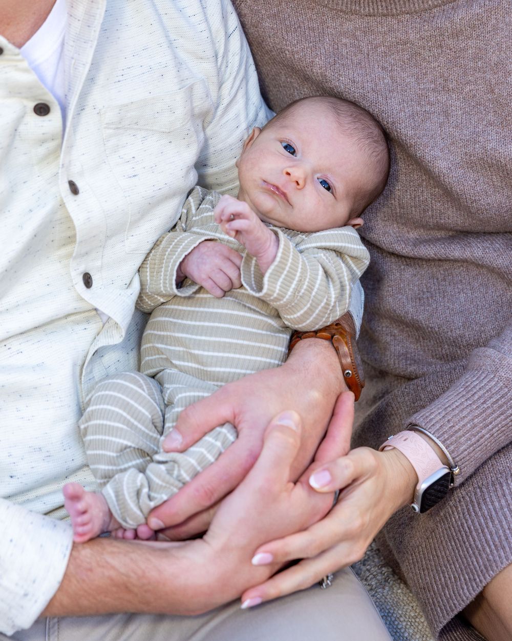 A baby being cradled in his parent's arms while wearing a striped onesie during a newborn photography session in Stow, MA