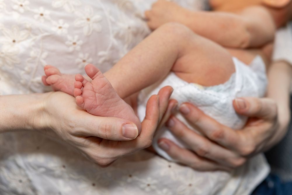 A mom gently cradles her newborn and hold his tiny feet during a newborn portrait photography shoot in Sudbury, MA.