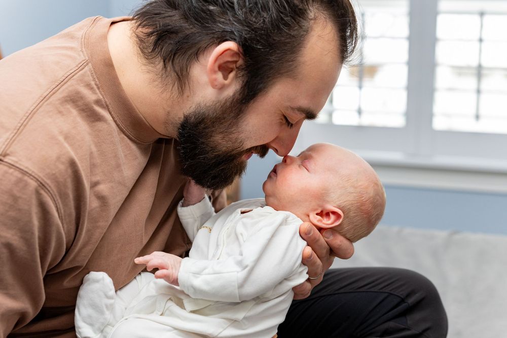A father tenderly cradles his newborn baby during newborn lifestyle portrait session by Lisa West Photography serving Boston and Metrowest.