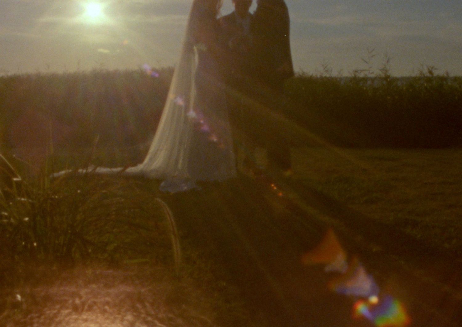 Romantic wedding couple embraces under a floral arch in an intimate woodland garden setting.