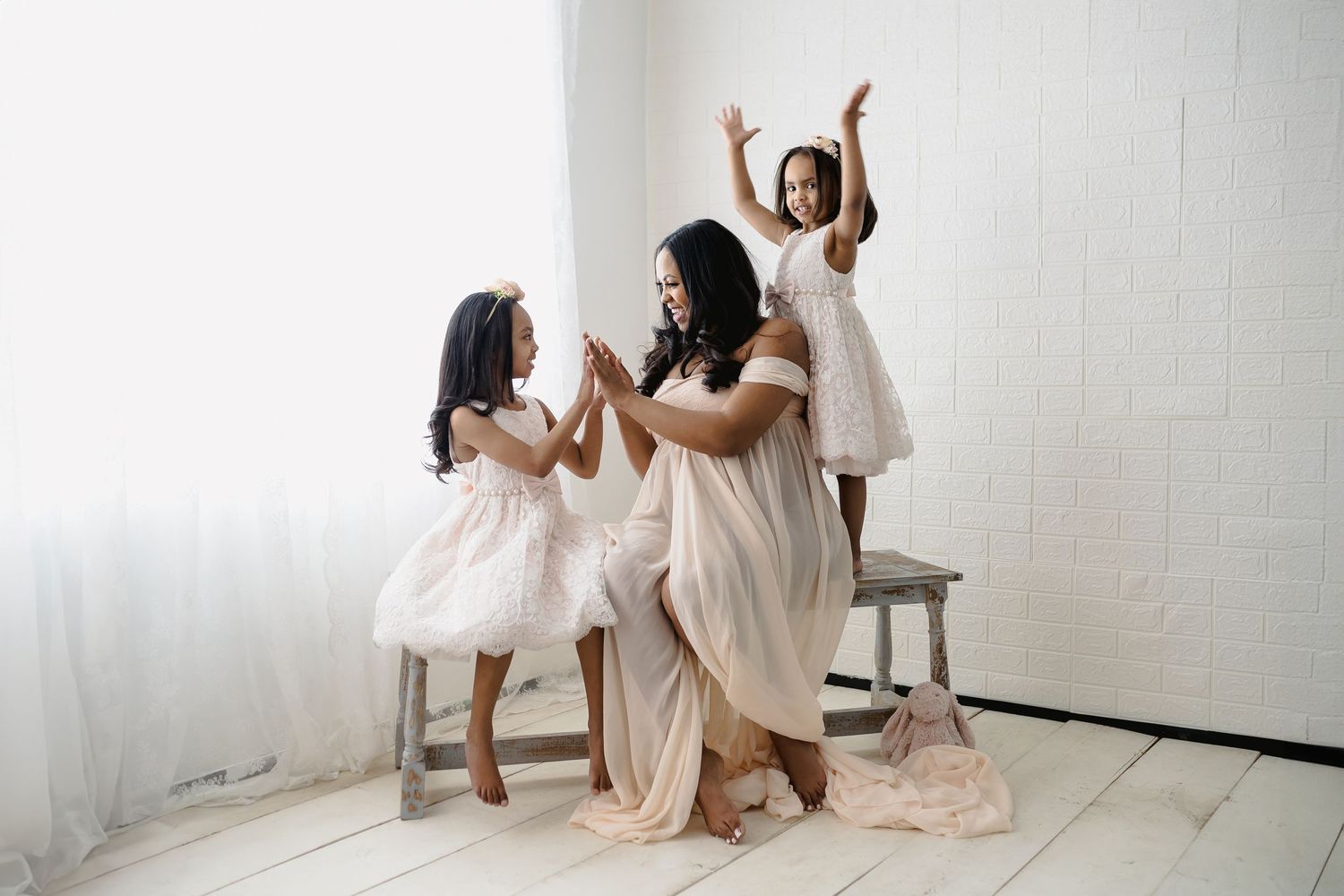 Joyful family bonding moment in white dresses against minimalist white backdrop.
