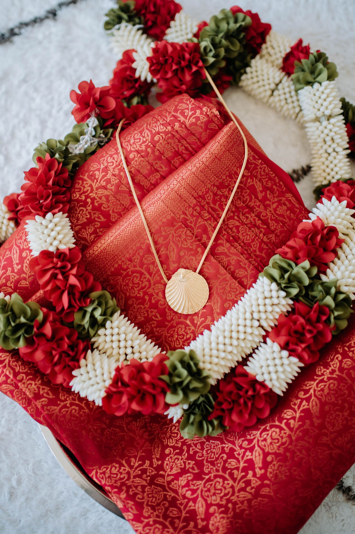 Red and white floral decorations surround a traditional red silk sari with a delicate gold necklace.