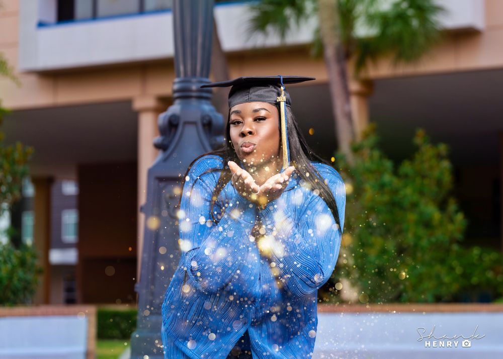 Graduate in sparkly blue dress poses playfully next to lamppost during outdoor graduation photoshoot.