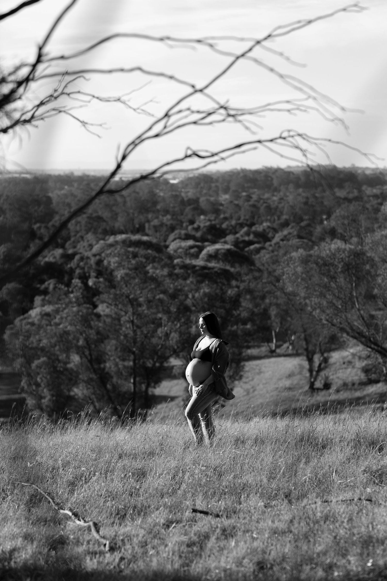 Silhouette of pregnant woman standing in field against dramatic landscape.