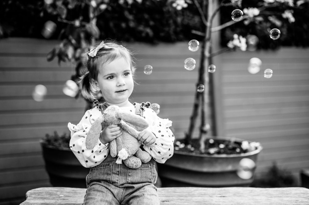 Young girl sitting on bench with bubbles around her at a nursery shoot, in Ashtead, Surrey