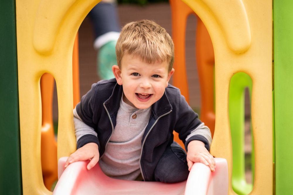 Young boy climbing up a slide smiling at the camera during a nursery photoshoot, in Ashtead, Surrey