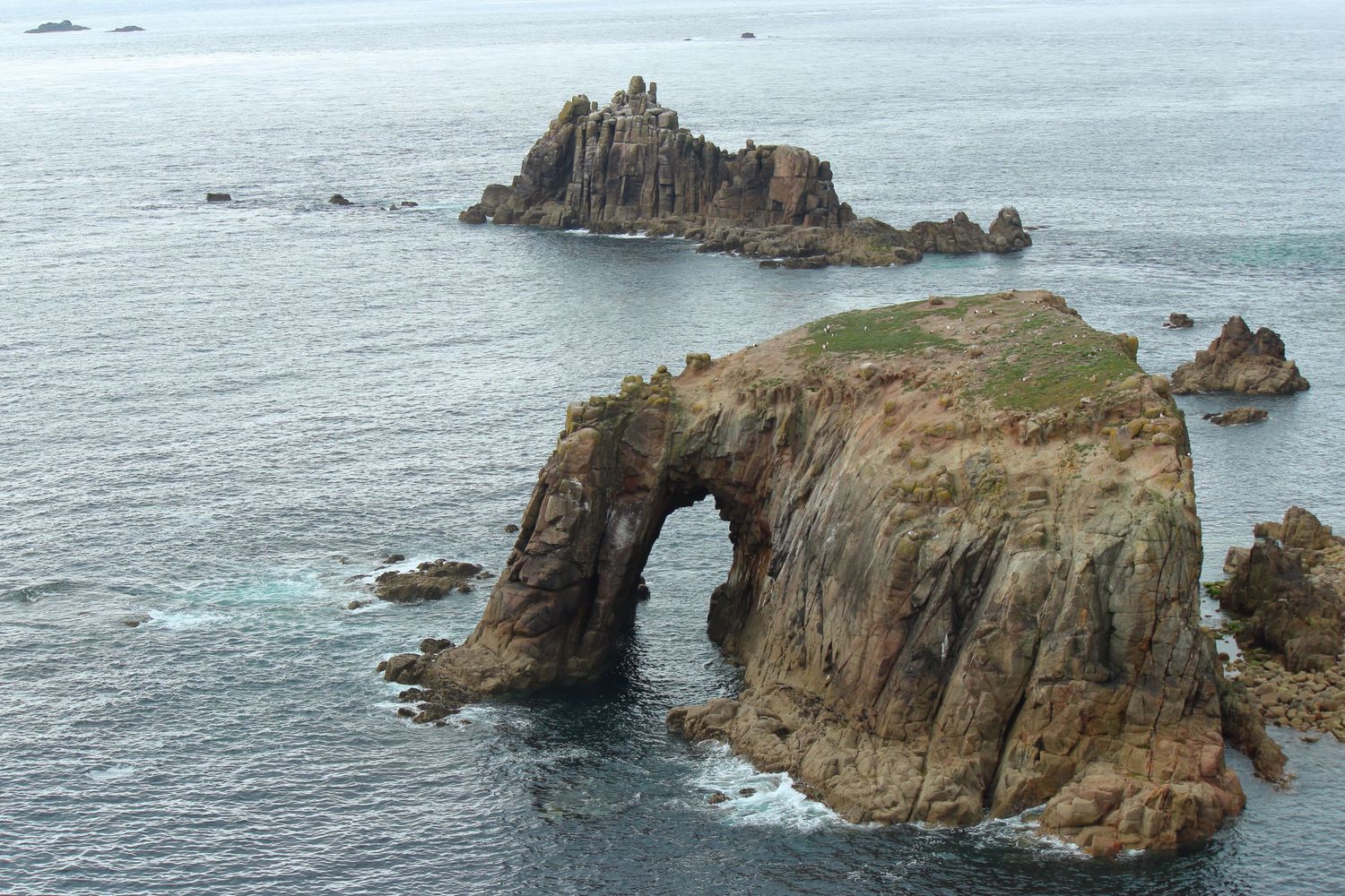 Enys Dodnan Arch, a stunning natural rock formation off the coast of Cornwall, standing gracefully against the backdrop of the deep blue sea