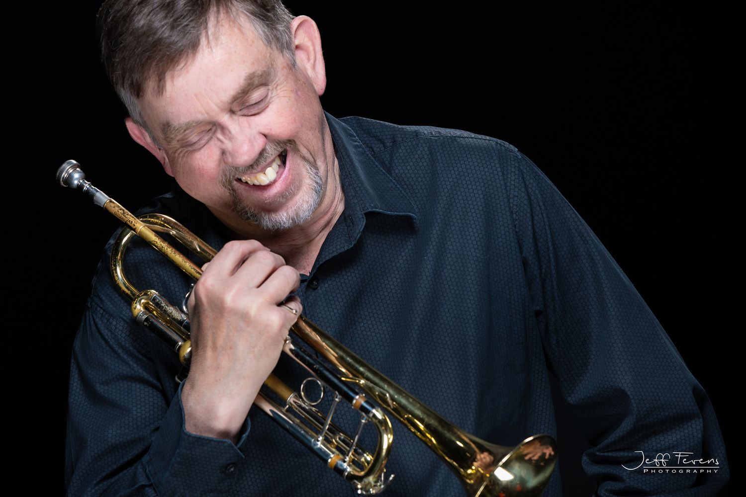 Black and White Headshot of a male trumpet player laughing.