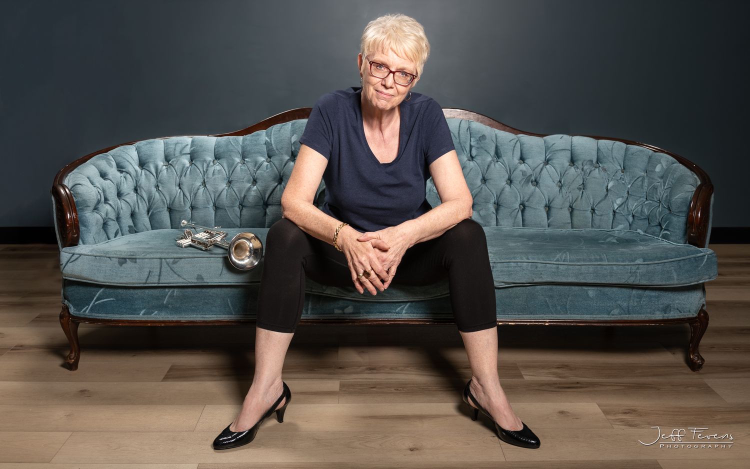 Colour image of a female trumpet player sitting on a chesterfield.