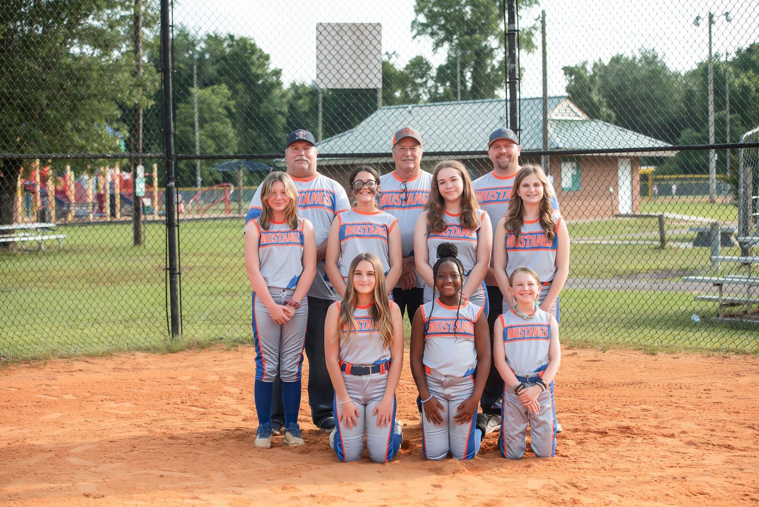 Softball team posing together on dirt infield for team photo.