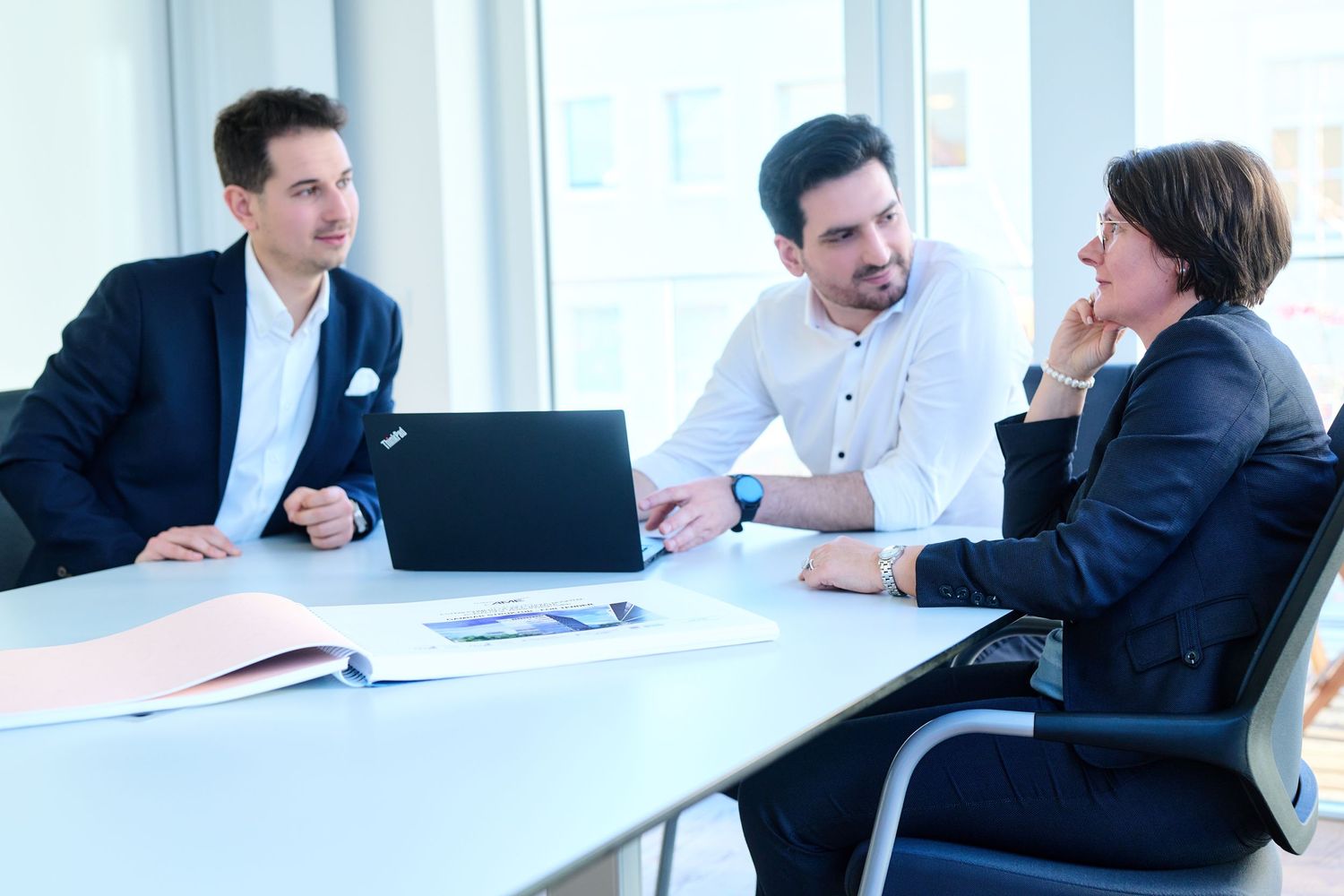 Three business professionals having a meeting around a table with a laptop.