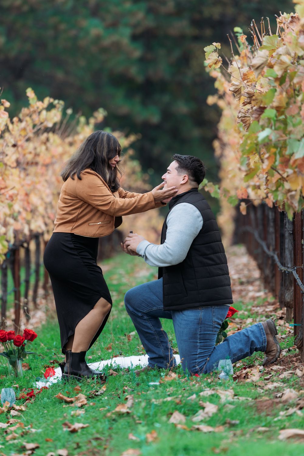 A couple shares a playful moment among autumn grapevines in a vineyard setting.
